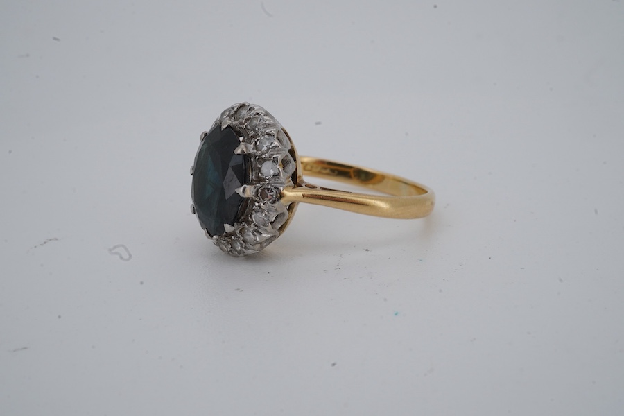 A sapphire and diamond ring, of cluster design, set with a cushion-shaped sapphire weighing approximately 2.20 carats, within a border of single-cut diamonds totalling approximately 0.50 carats, mounted in gold and plati